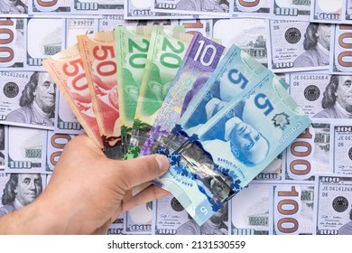 Calgary, AB. Canada. March 2, 2022. A Person Holding Canadian Banknotes On A Background With American Dollars. Concept: Currency Exchange Services And Rate Of Inflation