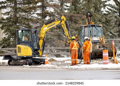 Calgary, Alberta, Canada. Apr 21, 2022. A Yanmar VIO35 Mini Excavator With Hydraulic Thumb And Dozer Blade Digging On The Ground With Some Construction Workers Around During The Winter. 