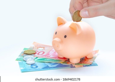 Calgary, Alberta, Canada. Dec 7 2020. A Person Saving Money On A Piggy Bank Canadian Currency. Canadian Bill And Coin On A White Background. Concept: Saving Money