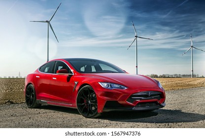 Calgary, Alberta / Canada November 1st 2019 : Photograph of a red Tesla model S in front of a windmill field.