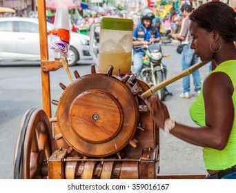 CALI, COLOMBIA - SEPTEMBER 9, 2015: Woman is squeezing sugar cane juice using old wooden machine on a street in the center of Cali.