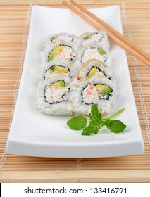 California Roll Sushi On White Plate With Chopsticks On Bamboo Mat