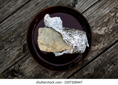 California Style Burrito In Flour Tortilla Wrapped In Foil On Plate (Overhead)