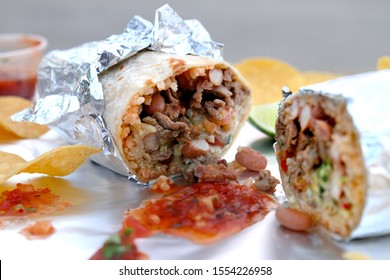 California Style Burrito Wrapped in Foil Surrounded by Chips and Salsa