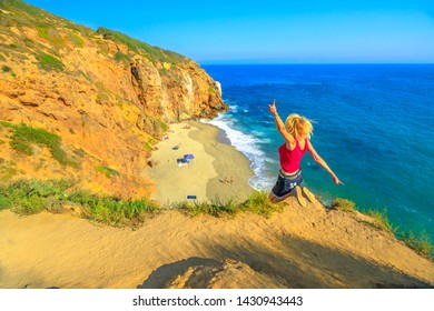 California travel destination concept. Lifestyle woman jumping on Pirates Cove promontory, a small cove on west side of Point Dume, Malibu coast in CA, United States. Jumper in Californian West Coast.