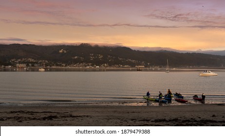 California, United States - December 
12, 2020: People taking kayaks at sunset time on the peaceful Pillar Point Harbor Beach, Half moon bay.