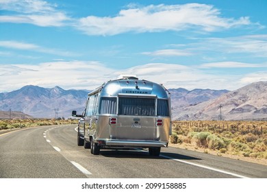 California USA 05-01-2021-Airstream Camper on two laned highway driving through sagebrush toward mountain range with electrical highlines - rear view.