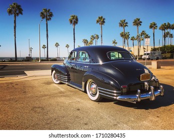 California, Year 2017: Old American Car On A California Beach. Classic Black Car And Palm Trees On The West Coast.