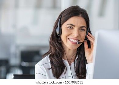 Call center agent with headset working on support hotline in modern office with copy space. Portrait of mature positive agent in conversation with customer over headset looking at camera.