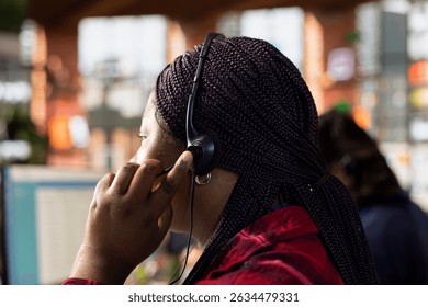 Call center agent in office using headset mic to answer customers questions, close up. Woman in customer support workspace in front of PC using audio headphones microphone to talk with clients