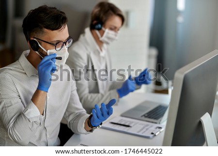 Call center agent using computer and communicating with customers while wearing protective face mask in the office. 