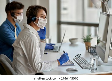 Call center agents wearing protective face masks while working on computer and communicating with customers during coronavirus epidemic. Focus is on woman.  - Powered by Shutterstock