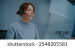 Call center: Close up of positive Caucasian female helpdesk specialist talking on headset with customer, working on computer, providing online assistance. Team of technical support operators working.