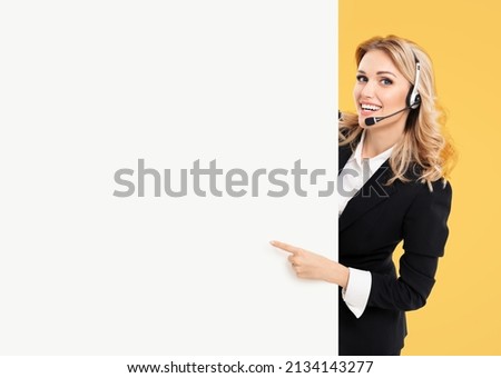 Call center. Customer support service female phone operator or sales agent in headset, confident suit standing behind signboard with copy space area for text, isolated on yellow background