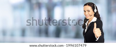 Call center. Face portrait of customer support phone advertiser sales operator in headset, showing thumbs up hand gesture. Answering service centre female phone worker over blurred office background.