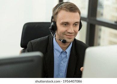 Call center male worker at work. Smiling male customer support operator in normal suit with headset working in the office. Contact center and customer service by headphone concept