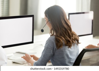 Call center operator in wireless headset with microphone using computer, looking at blank white screen mock up, busy female employee working in customer support service office, consulting client