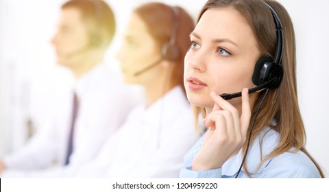 Call center operators. Focus on young cheerful smiling woman in headset. Business and customer service concepts