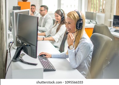 Call center operators.Young beautiful business woman with headset working on computer in office with colleagues in the background. - Powered by Shutterstock