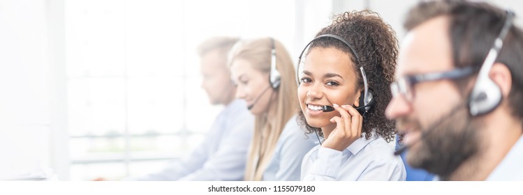 Call center worker accompanied by her team. Smiling customer support operator at work. Young employee working with a headset. - Shutterstock ID 1155079180