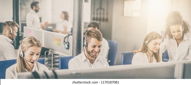 Call center worker accompanied by his team. Smiling customer support operator at work. Young employee working with a headset.