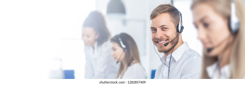 Call center worker accompanied by his team. Smiling customer support operator at work. Young employee working with a headset.