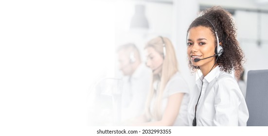 Call center worker accompanied by her team. Smiling customer support operator at work. Young employee working with a headset. - Shutterstock ID 2032993355