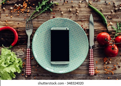 Call for delivery. Top view of plate and smart phone laying on the rustic wooden desk with vegetables around - Powered by Shutterstock