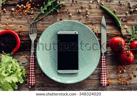 Call for delivery. Top view of plate and smart phone laying on the rustic wooden desk with vegetables around