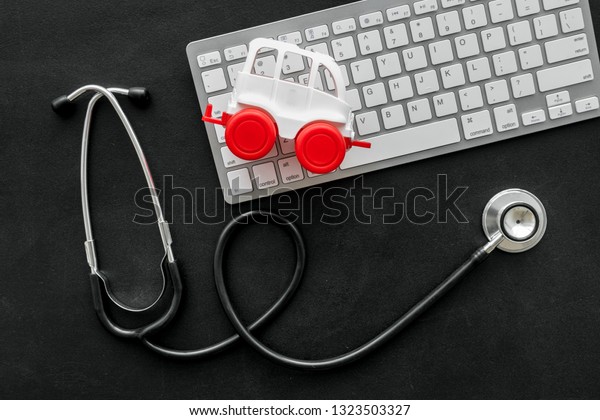 Call doctor\
online concept. Ambulance vehicle toy near computer keyboard and\
stethoscope on black background top\
view