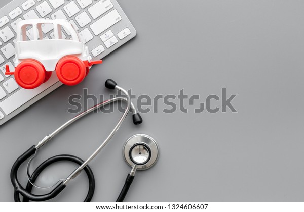 Call doctor online concept. Ambulance vehicle toy\
near computer keyboard and stethoscope on grey background top view\
space for text