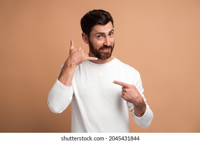 Call Me. Portrait Of Cheerful Handsome Man Standing With Telephone Hand Gesture And Smiling To Camera, Flirting Offering To Contact By Phone. Studio Shot Isolated On Beige Background 