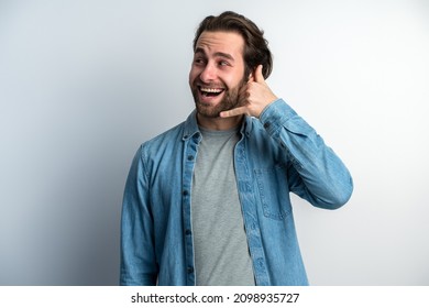 Call Me. Portrait Of Cheerful Handsome Man In Denim Shirt Standing With Telephone Hand Gesture And Smiling, Offering To Contact By Phone. Studio Shot Isolated On White Background 