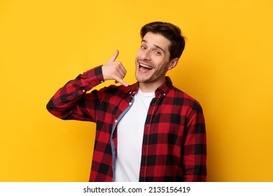 Call Me. Portrait of young smiling excited man making contact sign gesture with hand standing on yellow studio wall, posing looking at camera. Communication And Mobile Cellular Connection Concept.