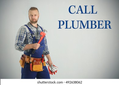 Call Plumber. Handsome plumber with pipe wrench and gloves on light background