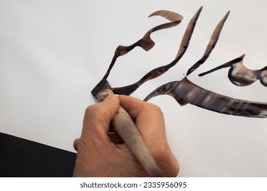 A calligrapher writing with pen and ink. man hands writing arabic calligraphy with ink. Arabic and Persian calligraphy. Written in Arabic, "In the name of God"