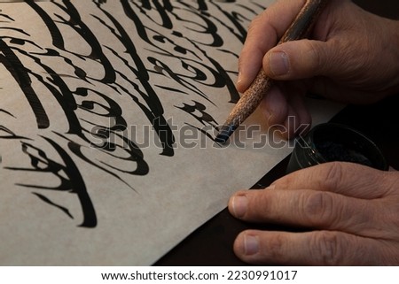 A calligrapher writing with pen and ink. man hands writing arabic calligraphy with ink. Arabic and Persian calligraphy. Abstract and unclear writing. A writing of repeating the letters 