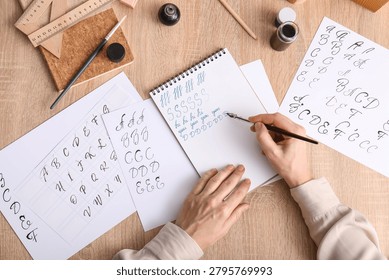 Calligraphy practice session with hand writing alphabet letters and ink pen on wooden desk, creative learning and artistic development
