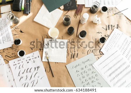 Calligraphy sheets, nibs, paper, ink and pens on a kraft background. Lettering calligraphy workshop. Letters of the English alphabet written with a paint brush. Concept hobby. top view, flat lay.