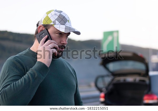 Calling car service, assistance or  tow truck
while having troubles with his car. Man calling road assistance on
the highway.