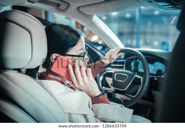 Calling children. Dark-haired woman calling her\
children while driving home from\
work