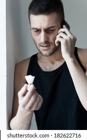 Calling to drug dealer. Frustrated young man holding a pack with heroin and talking on the mobile phone
