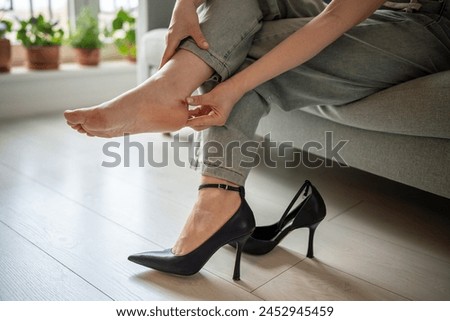 Callus blister on heel from tight shoes. Woman feet in pain after wearing high heeled shoes after walking. Female touching her ankle with sore. Corns, blisters on foot. Uncomfortable shoes problems.