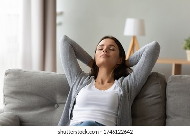Calm 20s woman resting seated on couch in light warm living room put hands behind head enjoy fresh air-conditioned climate control, meditation, inner balance, relaxation at home free lazy day concept - Shutterstock ID 1746122642
