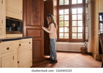 Calm Adult Woman Standing In The Kitchen And Taking Food From The Big Wooden Cupboard