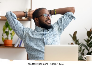 Calm african american business man take break at workplace relaxing finished work, happy black professional employee enjoy success rest from computer feeling stress relief peace of mind sit at desk