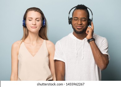 Calm African American man in glasses and Caucasian woman in headphones enjoying music with closed eyes, diverse friends, couple listening to favorite song, good sound, isolated on studio background - Powered by Shutterstock