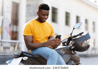 Calm african american man using mobile phone while relaxing at the street after motorbike riding. People lifestyle concept  - Powered by Shutterstock