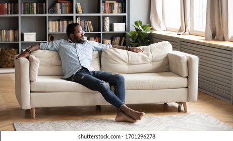 Calm African American Young Man Sit Relax On Comfortable Couch In Living Room Look In Distance Thinking, Relaxed Biracial Millennial Male Rest On Sofa At Home, Breathe Fresh Air, Stress Free Concept