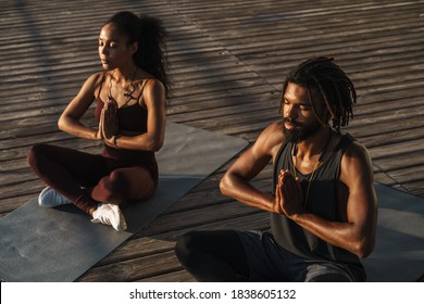 Calm afro american couple doing yoga exercises outdoors, sitting on a fitness mat - Powered by Shutterstock